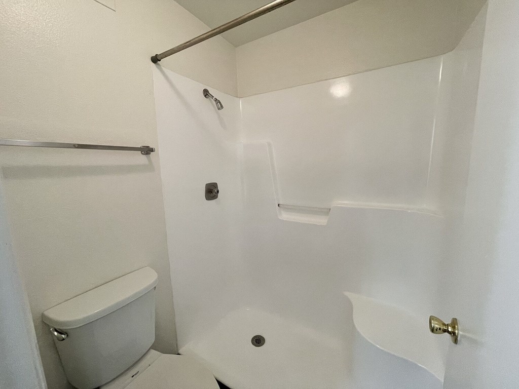 A white bathroom with a toilet, a shower, and a towel bar.